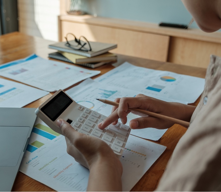 Valuer advisor calculating financial data using a calculator in a workspace filled with reports and documents